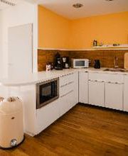 Eine Küchenzeile mit Ofen, Mikrowelle, Wasserkocher, Kaffeemaschine und Mülleimer.