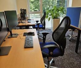 Teilnehmerraum mit mehreren Arbeitsplätzen, jeweils mit zwei Bildschirmen, Bürostuhl, Tastatur, Maus