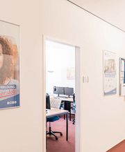 Flur mit Plakaten und Pinnwand an der Wand. Blick in einen Schulungsraum.