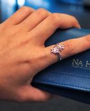 Woman's hand wearing a double-honu cuff bangle bracelet and double honu bypass ring, holding a Na Hoku jewelry travel pouch. Background: airport hall.