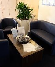 Sitzgruppe bestehend aus 2 blauen Sesseln und einem Sofa. Ein Beistelltisch mit Süßigkeiten, dahinter eine Topfpflanze und mehrere Schränke.