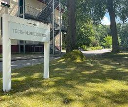 Ein Rasen mit zwei Bäumen vor einem Gebäude. Ein Schild mit der Aufschrift "Technologiezentrum" steht auf dem Rasen.