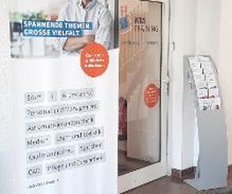 Eingangstür und Werbeaufsteller WBS TRAINING, rechts ein Flyerständer.