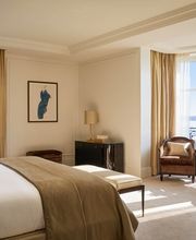 Spacious bedroom with king bed, French windows, and soft beige decor at The Woodward Geneva.