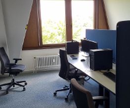Ein Schulungsraum mit mehreren Arbeitsbereichen, die durch blaue Trennwände voneinander getrennt sind. Jeder Arbeitsplatz besteht aus 2 PC-Bildschirmen, Tastatur und Maus sowie Headset und blauen Trennwänden.