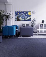 Heller Aufenthaltsraum mit 2 blauen Sesseln und weißen Beistelltisch, 2 graue Sofas und einem kunstvollem Bild an der Wand. Im Raum stehen einige, grüne Zimmerpflanzen.