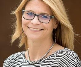 Eine Frau mit blonden Haaren, Brille und gestreiftem Oberteil.