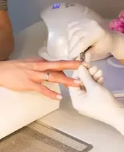 Das Bild zeigt eine professionelle Maniküre, bei der die rechte Hand einer Frau gepflegt und kosmetisch behandelt werden. Die Hand liegt stabil auf einer sauberen Unterlage, während eine Fachkraft die Nägel formt, vorbereitet oder pflegt. Die Szene wirkt ruhig, hygienisch und präzise. Der Fokus liegt auf den Händen der Kundin und den professionellen Handgriffen der Maniküre-Spezialistin, die typische Werkzeuge und Techniken für die Nagelbehandlung einsetzt.