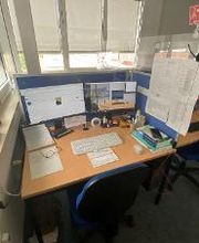 Ein Arbeitsplatz mit 2 Bildschirmen, einem Bürostuhl, Tastatur, Maus und Headset. Mehrere Dokumente liegen am Arbeitsplatz