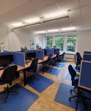 Ein Schulungsraum mit vielen Arbeitsplätzen. Alle Arbeitsplätze sind durch blaue Trennwände abgetrennt und sind mit 2 Monitoren sowie Tastatur, Maus und einem Headset ausgestattet.