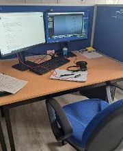Arbeitsplatz mit 2 Bildschirmen, einer Maus, einer Tastatur und einem Headset. Auf dem Tisch liegen mehrere Dokumente.