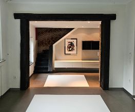 Offener Wohnraum mit Fachwerk-Elementen: Minimalistisches Interior Design mit dunklen Holzbalken, schwarz-weißem fugenlosen Boden und indirekter Beleuchtung.