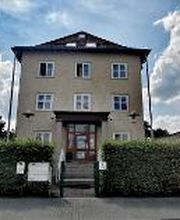 Gelbes Gebäude mit grüner Hecke und Treppen zum Eingang