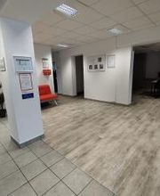 Eingangsbereich mit Säule. Links ein Regal mit Zimmerpflanzen, rechts der Blick auf mehrere Arbeitsplätze.