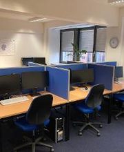 Schulungsraum mit mehreren Arbeitsplätzen mit jeweils 2 Bildschirmen, einem Bürostuhl, Tastatur, Maus und Headset.