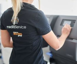 mediaService Bremen | Full-Stack Werbeagentur - Eine Mitarbeiterin in dunkler Arbeitskleidung bedient das digitale Touchscreen-Bedienfeld einer modernen, professionellen Großformat-Druckmaschine in einer Druckerei.