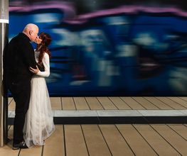 Hochzeitsfotograf Tom Maiwald - Urbanes Hochzeitsfoto eines Paares vor einem vorbeifahrenden Zug. Kreative Hochzeitsfotografie in Leipzig verbindet Bewegung, Stadtarchitektur und einen ruhigen Moment zu zweit.