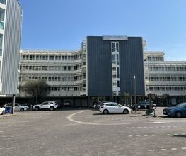 Außenansicht vom Gebäude mit heller Fensterfassade und Parkmöglichkeiten.