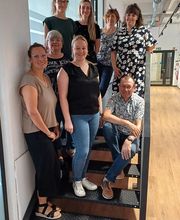 Gruppenbild vom Team der Region Leipzig. Die Personen sitzen und stehen auf einer Treppe im hellen Flur.