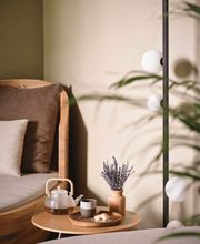 A cozy lounge chair with a tea set, candle, and lavender arrangement on a wooden side table.