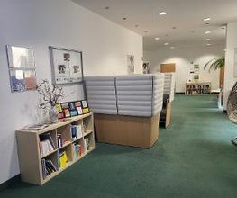 Eingangsbereich mit Sitzbereich. Links ein Bücherregal, rechts ein Hängesessel. Im Hintergrund ein weiteres Regal und Plakate.