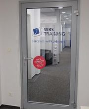 Eine Glastür mit der Aufschrift "WBS TRAINING" und "Herzlich Willkommen".