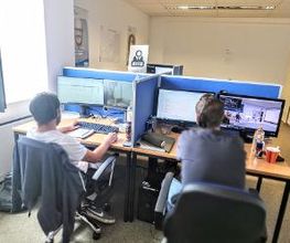 zwei Teilnehmer sitzen am Rechner und arbeiten am Computer mit zwei Bildschirmen und kommunizieren über Headset