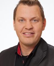 Mann mit einem schwarzen Sakko schaut freundlich in die Kamera.