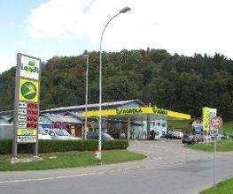 AGROLA Tankstelle in Wolhusen mit TopShop und Landi Laden. Einfahrt zur Tankstelle, links daneben Schild mit Landi Logo, AGROLA Diskus Logo und digitale Preisanzeige Schild