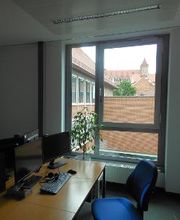 Ein Arbeitsplatz mit zwei Monitoren und einer Tastatur und Maus vor einem Fenster.