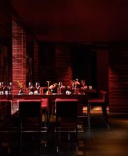 Dimly lit red and black interior of L’Atelier Robuchon Geneva, featuring counter seating and open kitchen.