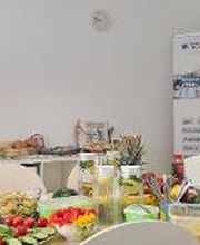 Gedeckter Frühstückstisch im Aufenthaltsraum. Dahinter ein Plakataufsteller.