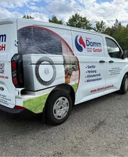 Weißer Kleintransporter mit markanter Beschriftung, grünen Designelementen und großflächigen Grafiken. Die rundum platzierte Fahrzeugwerbung präsentiert Marke, Leistungen und Kontaktdaten übersichtlich und einprägsam.