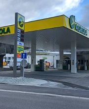 AGROLA Tankstelle in Zell, Luzern, Einfahrt im Vordergrund mit Pfeilmarkierung, links Totem mit AGROLA Diskus Logo, digitaler Preisanzeige, AdBlue, TopShop Logo darunter; im Hintergrund TopShop