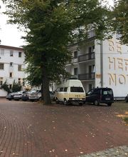 Außenansicht vom Gebäude mit einigen Bäumen und Autos davor.