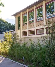 Gebäudeansicht des Fröbel-Kindergartens Essener Straße mit großen Fenstern, Klinkerfassade und bepflanztem Vorgarten entlang des Gehwegs.
Fröbel-Kindergarten Essener Straße, Hamburg, © Fröbel, Foto: Martin Arnold. Alle Rechte vorbehalten.