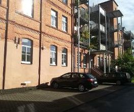 Backsteingebäude mit Balkonen und einem Parkplatz davor.
