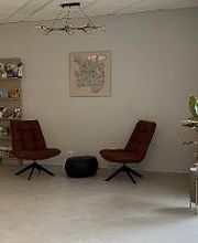 Foyer mit gemütlicher Sitzgruppe bestehend aus zwei dunkelroten Sesseln, einem Sitzkissen und einem Bild an der Wand. Daneben ein Regal sowie einige grüne Zimmerpflanzen.