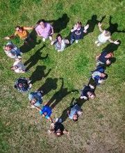 Ein Bild aus der Vogelperspektive. Die Mitarbeiter des Standortes haben sich auf einer Wiese in Form eines Herzens aufgestellt.
