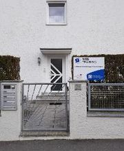 Eingangstor zum weißen Haus mit Hecke und WBS TRAINING Schild.