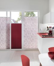 Eine moderne Küche mit halbtransparenten, gemusterten Plissees in Rot und Weiß, die für eine warme und stilvolle Atmosphäre sorgen.