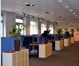 Trainingsraum mit Fachablagen vor den Schreibtischen mit je zwei PC-Bildschirmen. Auf den schränken stehen schöne, grüne Zimmerpflanzen.