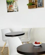 Heller Aufenthaltsbereich mit zwei kleinen, runden Tischen und je zwei Stühlen.