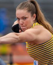 Eine Athletin befindet sich während eines Leichtathletik-Wettkampfs in einer kraftvollen Bewegungsphase. Die Spannung im Körper zeigt hohe Konzentration und Technik.