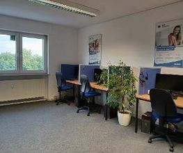 Drei Schreibtische mit Schreibtischstuhl, blaueen Trennwänden, Bildschirmen, Tastatur und Headset.