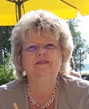 Bild einer blonden Mitarbeiterin mit Brille, die draußen unter einem gelben Sonnenschirm sitzt und in die Kamera schaut.