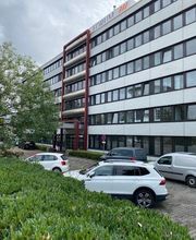 Mehrstöckiges Bürogebäude. Davor sind mehrere Parkplätze.