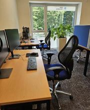 Teilnehmerraum mit mehreren Arbeitsplätzen, jeweils mit zwei Bildschirmen, Bürostuhl, Tastatur, Maus