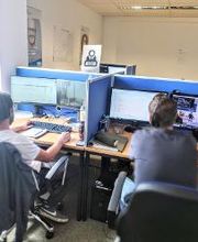 zwei Teilnehmer sitzen am Rechner und arbeiten am Computer mit zwei Bildschirmen und kommunizieren über Headset