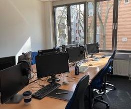 Schulungsraum mit einer großen Fensterfront und Schreibtischen die mit Bildschirmen, Tastaturen, Mäusen und Headsets ausgestattet sind.
